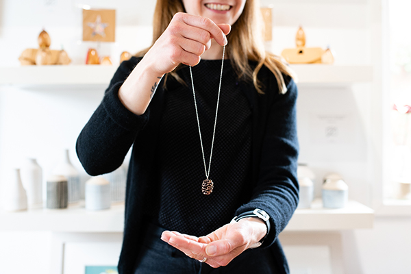 Sarah gallery owner holding a silver chain with a brown acorn necklace.
