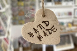 Cream handmade ornament on a piece of kraft coloured string, with embossed text painted reading hand made.