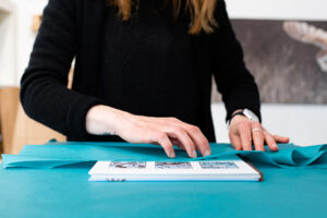 Sarah wistow gallery owner wrapping a book in turquoise sustainable tissue paper.