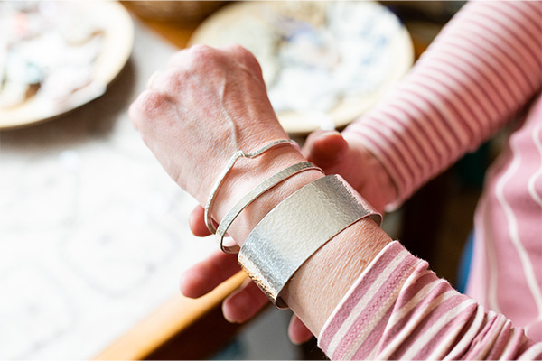 Hand featuring handmade silver bracelets one with a kink in for style, another thin band with a texture on and another with a thick band with texture.