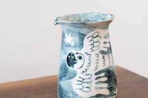 Handmade jug/vase featuring a illustrated bird with a unusual face. Featuring lots of blue and white colours with a rustic handmade feel.