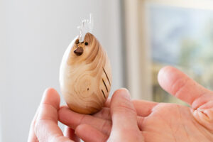 Handmade wooden egg with white mohawk being held in hands to show scale.